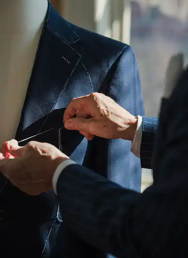 Tailor adjusting a dark suit jacket on a mannequin for a precise fit.