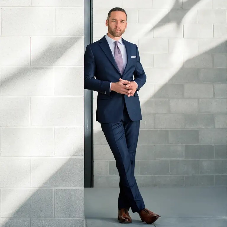 Elegant businessman in a navy suit posing confidently outdoors.